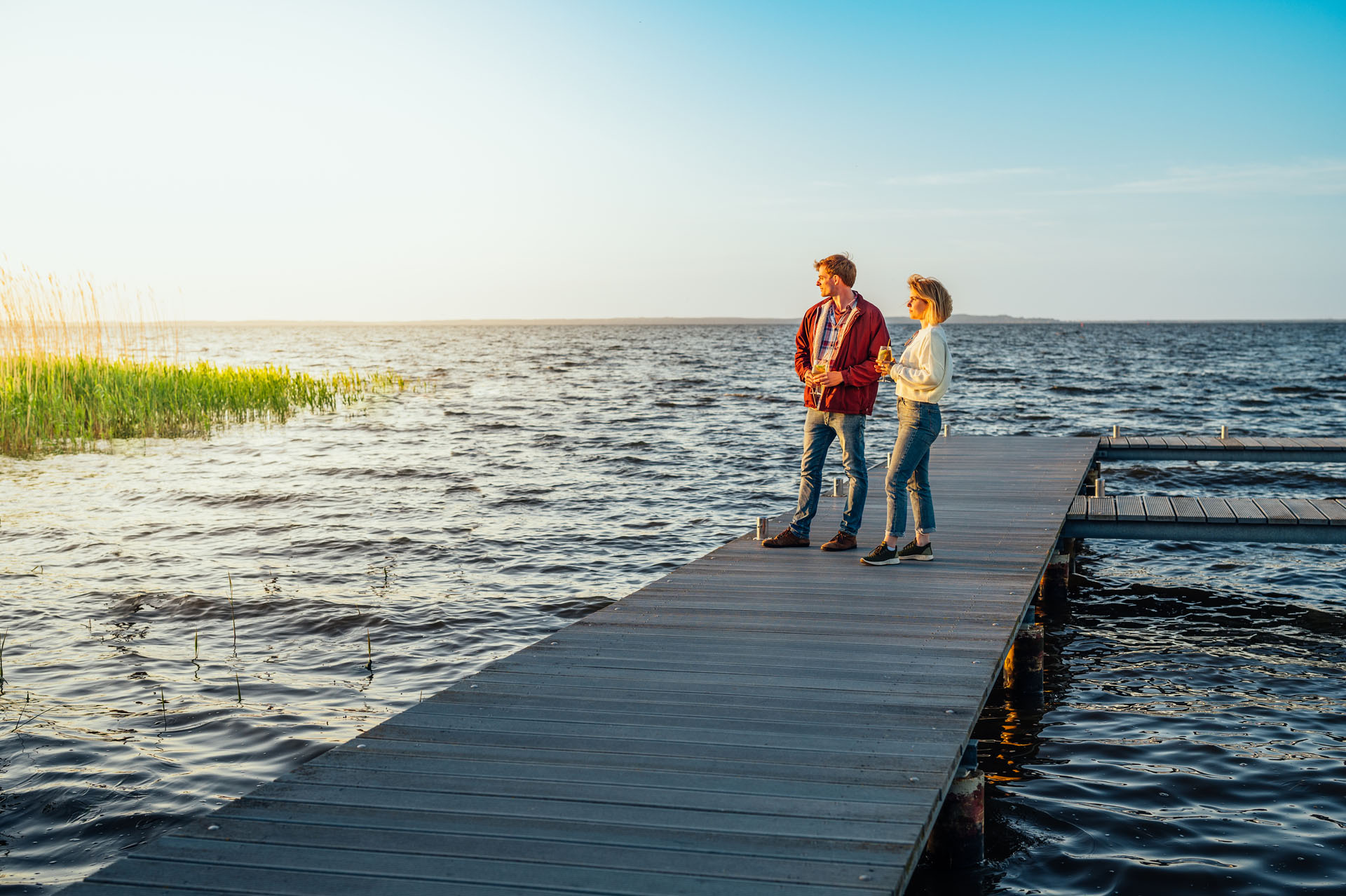 Couple stands on a jetty and looks at the sun